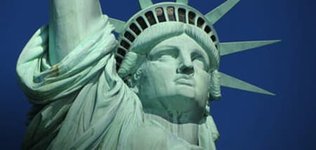 Close-up of the Statue of Liberty's head and upraised torch arm against a clear blue sky.