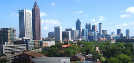 The Atlanta city skyline featuring multiple skyscrapers rising above green trees on a sunny day.