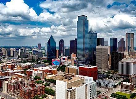 Expansive city skyline featuring diverse skyscrapers and buildings under a dramatic partly cloudy sky.