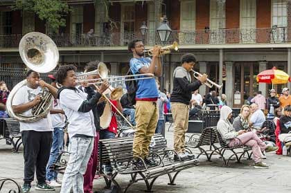 Young men's brass band plays tuba, trombone, and trumpet outdoors in a city square.