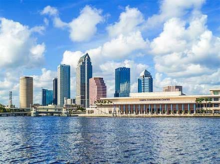 Modern city skyline by a blue waterfront under a partially cloudy sky.